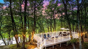 Una terrazza con posti a sedere all'aperto, circondata da alberi e con vista su un corpo d'acqua.