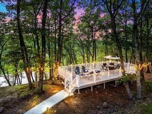 Eine Terrasse mit Sitzgelegenheit im Freien, umgeben von Bäumen und mit Blick auf ein Gewässer.