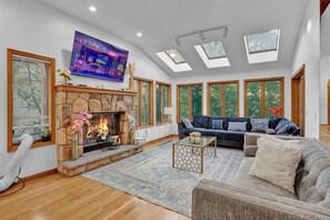 Ein geräumiges Wohnzimmer mit Kamin aus Stein, einer großen Couch, einem Couchtisch und einem an der Wand befestigten Fernseher.