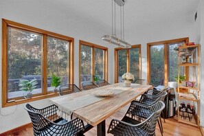 Ein Essbereich mit einem Holztisch, schwarzen Stuhlgestellen aus Draht und großen Fenstern.