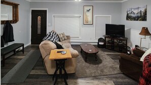 Ein Wohnzimmer mit Sofa, Couchtisch, Fernseher und Kunstwerken an den Wänden.