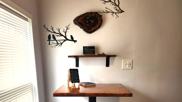 Ein Eckzimmer mit Holztisch, zwei Hocker, einer an der Wand befestigten Ablage und einem dekorativen Zweig.