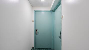 Un pasillo estrecho con una puerta azul turquesa, un suelo estampado y una lámpara en el techo.