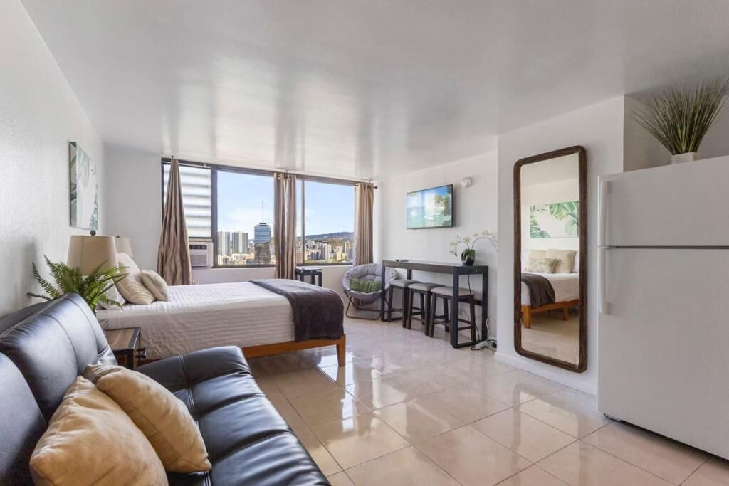 Een moderne hotelkamer met een bed, een sofa, een bureau en een groot raam met uitzicht op de stad.