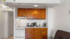 A compact kitchen with wooden cabinets, a microwave, a stove, and a coffee maker.