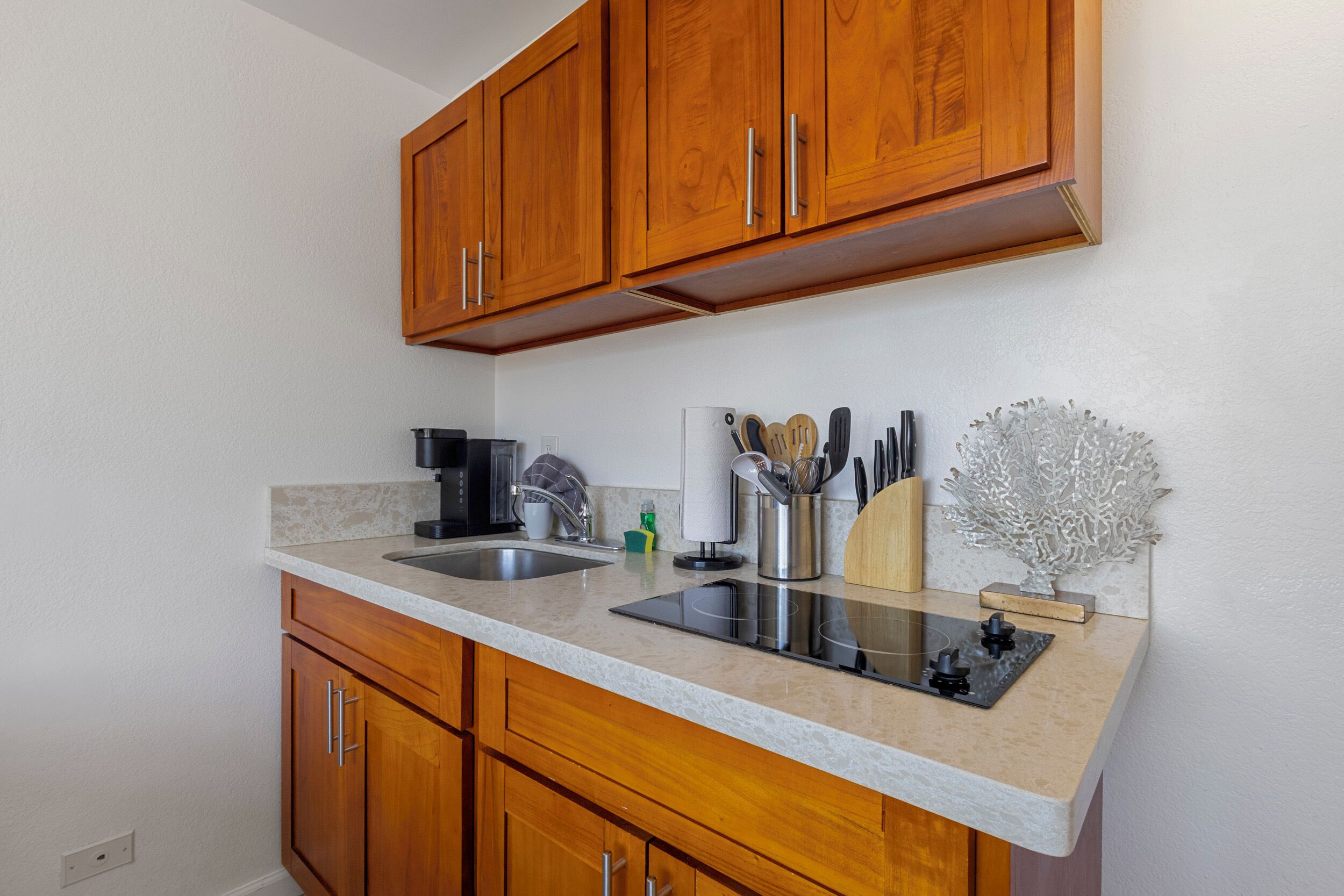 Una cocina con armarios de madera, un lavamanos de acero inoxidable, una estufa negra y varios utensilios de cocina.