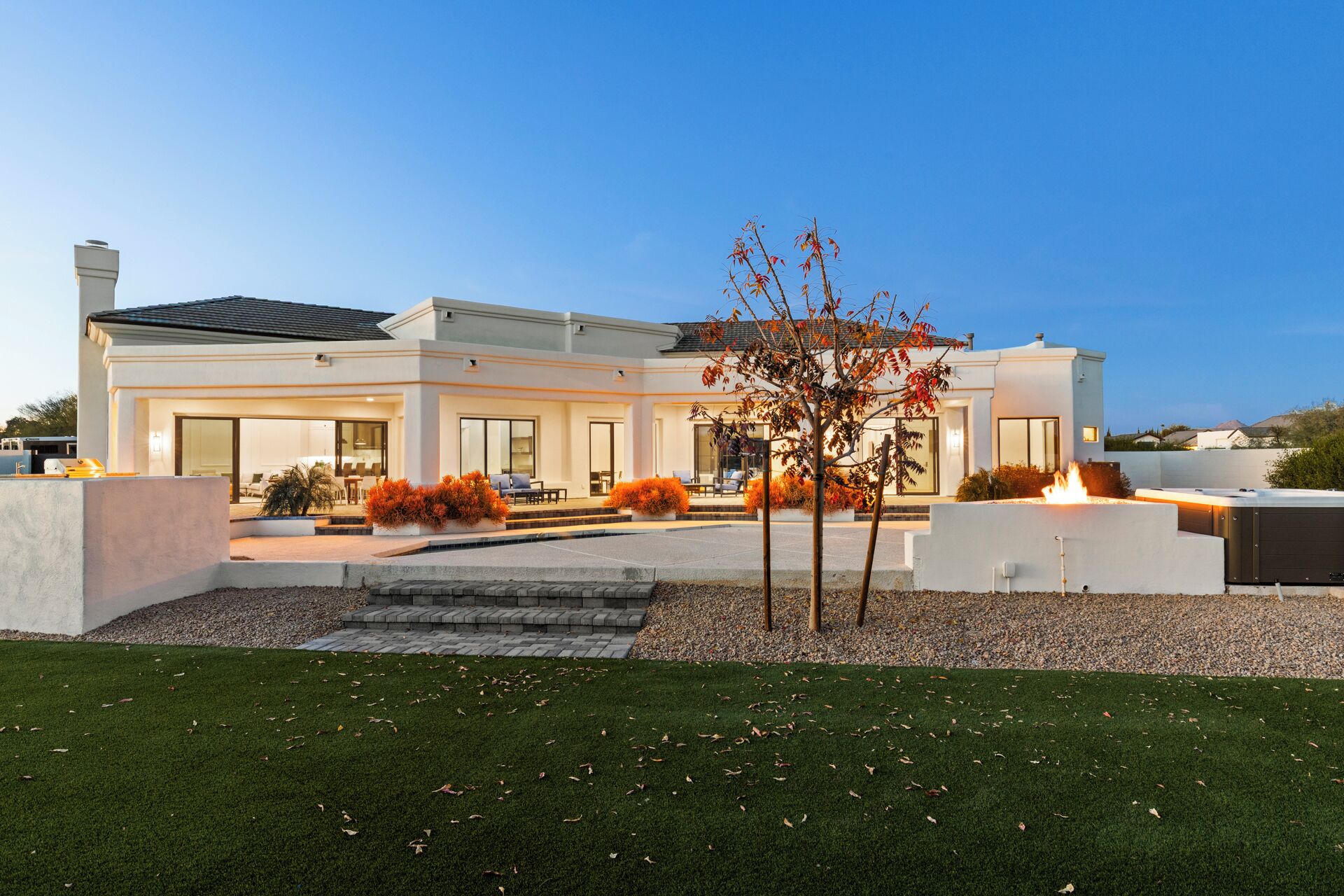 A modern two-story house with a covered patio, a fire feature, and a well-maintained lawn.