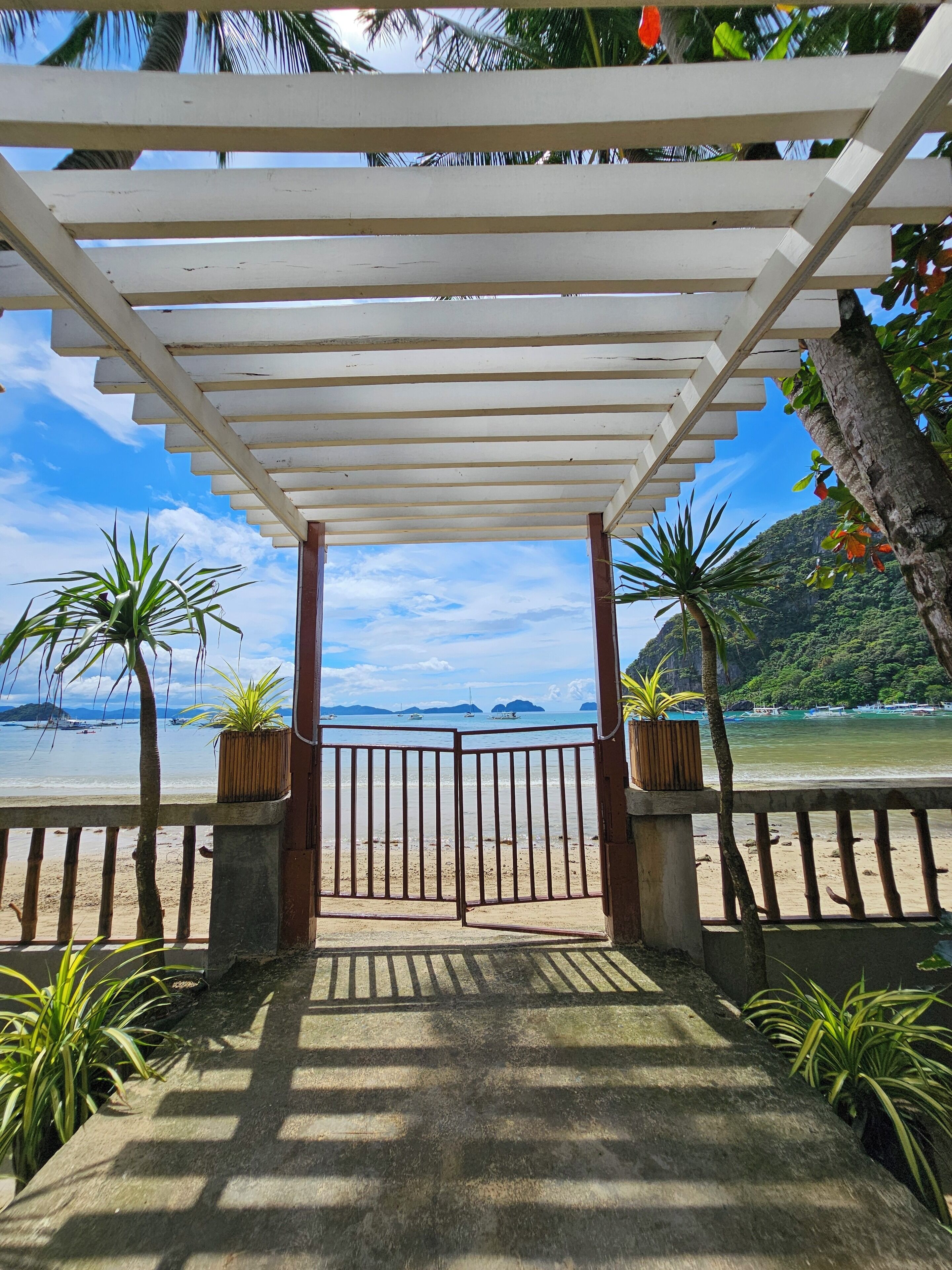 A covered walkway leading to a beach with a view of the sea and distant islands.