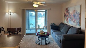 Ein Wohnzimmer mit Deckenventilator, einer Couch, einem Couchtisch und Blick auf das Wasser durch die Schiebetüren.