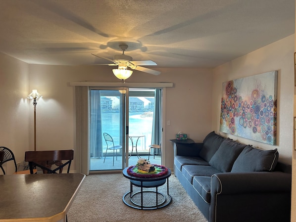 A living room with a ceiling fan, a sofa, a coffee table, and a view of the water through the sliding glass doors.