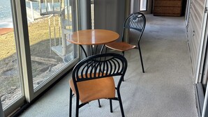 Ein Zimmer mit einer großen Schiebetür zum Balkon, einem runden Holztisch, zwei schwarzen Stühlen und einem Holzschrank.