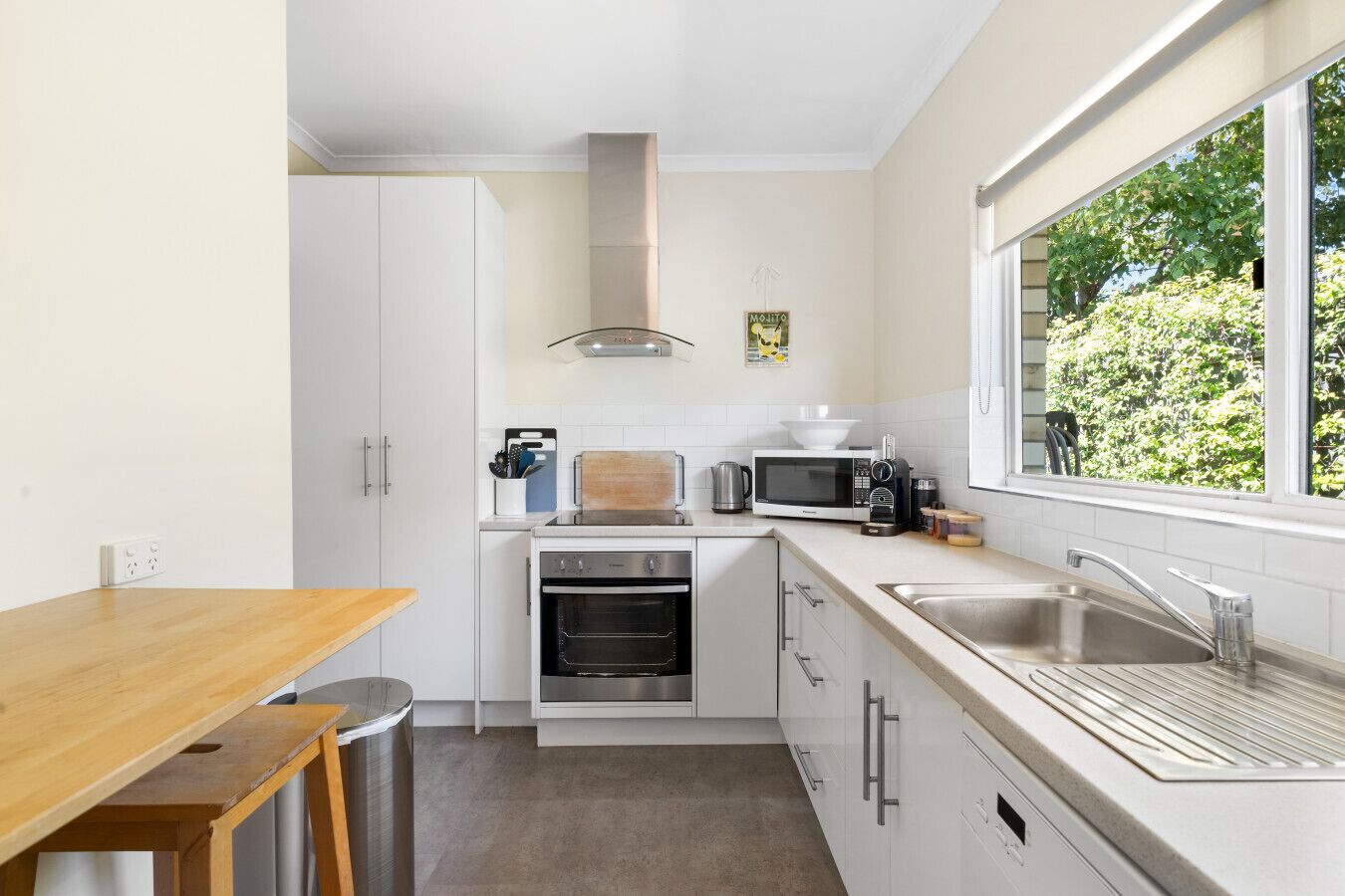 A compact kitchen with white cabinets, a microwave, a stove, and a sink. There is a window providing a view of greenery outside.