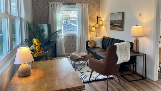 A cozy living room with a wooden table, a sofa, and a TV. There are two lamps on the table and a painting on the wall.