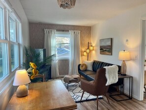 A cozy living room with a wooden table, a sofa, and a TV. There are two lamps on the table and a painting on the wall. - Cozy 1-bedroom apartment in quaint Minneapolis neighborhood (Minneapolis)