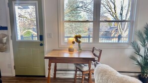 A dining area with a wooden table, chairs, a vase with flowers, and a view of trees through a window.