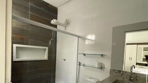 Casa de banho moderna com cabine de duche em vidro, sanita, lavatório com bancada de granito e espelho sobre o lavatório.