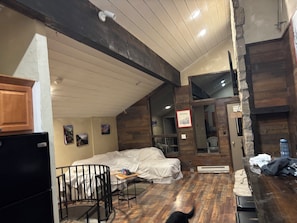 Une pièce rustique avec un plafond en bois, un lit, une petite table et un réfrigérateur.