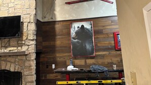 A room with a stone wall, a mounted TV, a wooden bench, a framed picture of a bear, and a red ski pole. - Cozy 2-bedroom condo with AC in pleasant Whitefish (Whitefish)