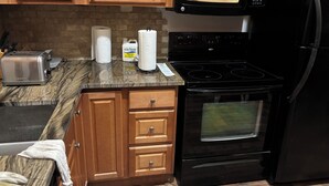 A kitchen with wooden cabinets, a black stove, a microwave, and a toaster. - Cozy 2-bedroom condo with AC in pleasant Whitefish (Whitefish)