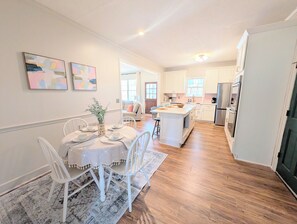 A modern kitchen with white cabinets, a central island, and a dining area with white chairs and a table. - Spacious 5-bedroom Master's Retreat, North Augusta. 8.7 mi. to Augusta National (North Augusta)
