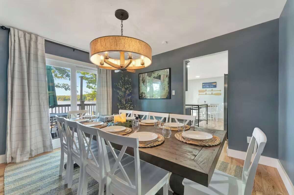 A dining area with a wooden table, white chairs, and a hanging light fixture.