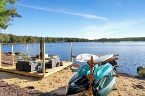 A lakeside deck with kayaks, a paddleboard, and outdoor seating. - Lakefront Beach Entry - Hot Tub, Movie Theater! (Tobyhanna)