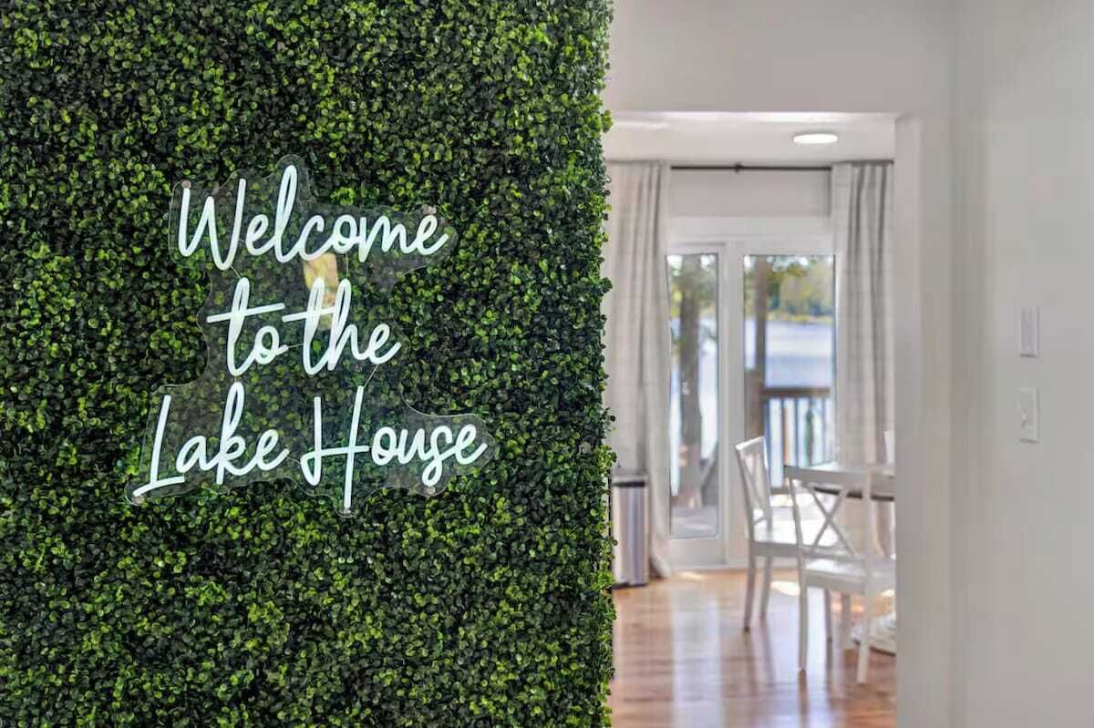 A welcome sign against a green wall, a wooden floor, and a view of a balcony with chairs.