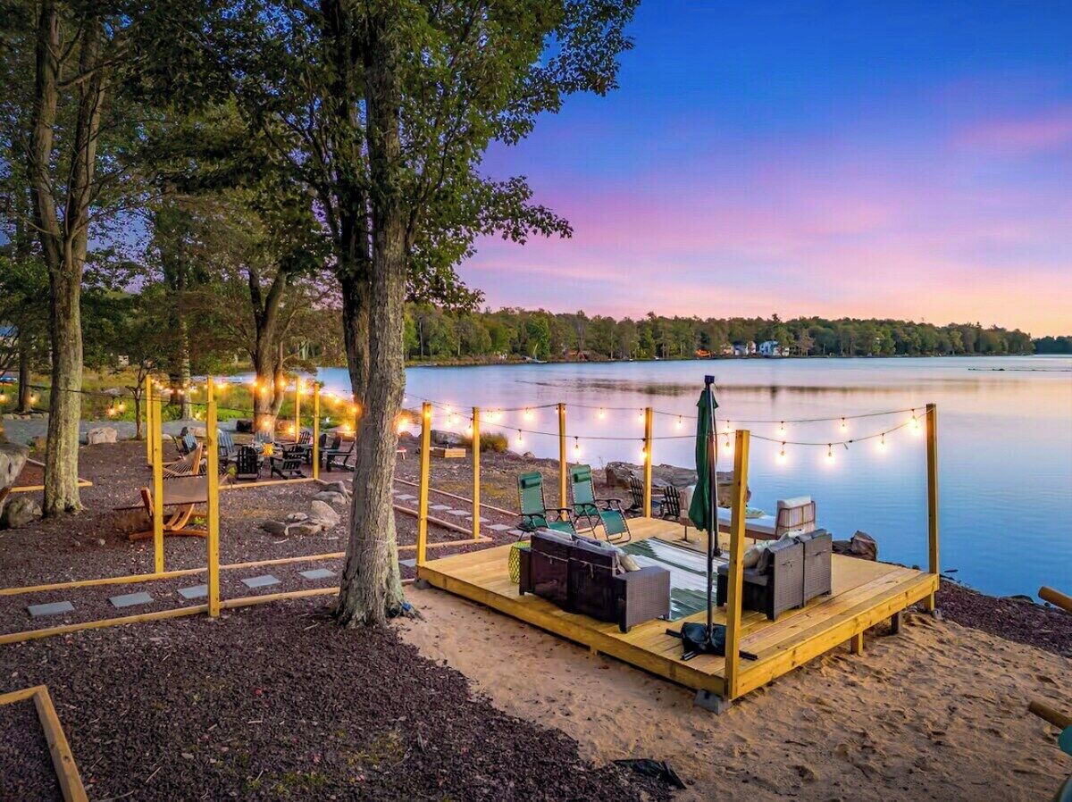A wooden deck with seating and string lights, overlooking a calm lake.