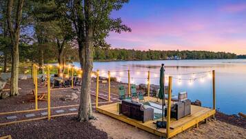 A wooden deck with seating and string lights, overlooking a calm lake.