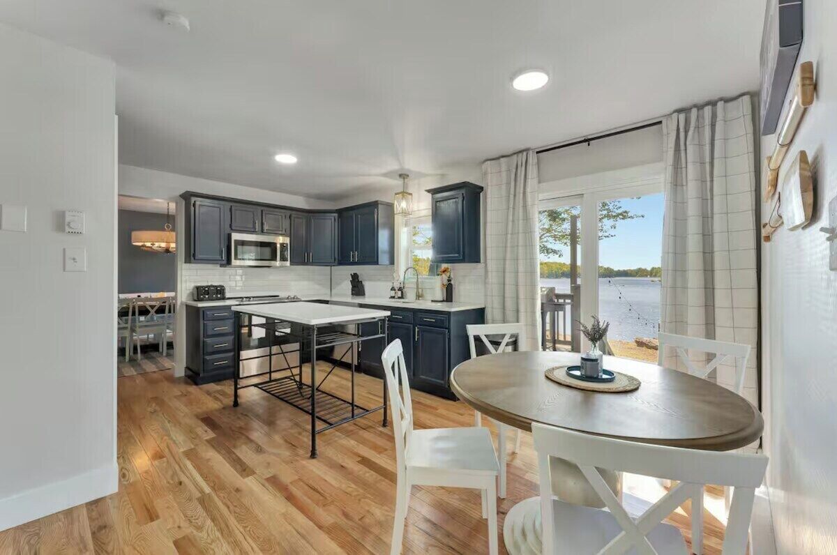 Una cocina moderna con armarios oscuros, una isla central y una zona de comedor con mesa y sillas.