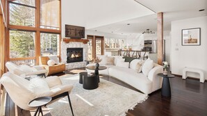 A spacious living room with a fireplace, large windows, and a modern kitchen in the background. - Snowmass Village Retreat, Pet-Friendly, Hot Tub, Game Room & Rooftop Deck Near Base Village (Snowmass Village)