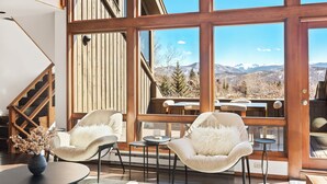 A modern interior with a wooden staircase, two plush chairs, a small table, and a large window offering a mountain view. - Snowmass Village Retreat, Pet-Friendly, Hot Tub, Game Room & Rooftop Deck Near Base Village (Snowmass Village)