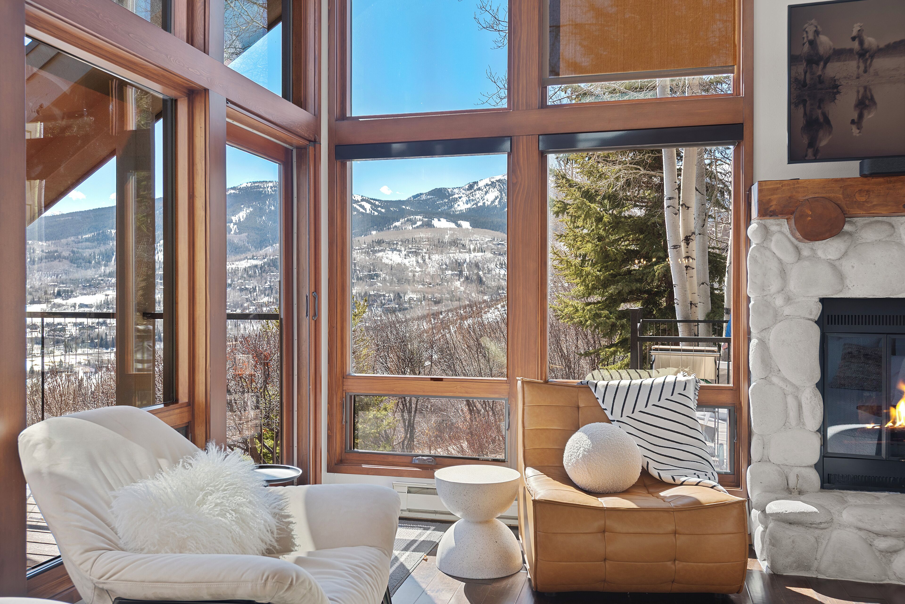 Une pièce chaleureuse avec de grandes fenêtres donnant sur les montagnes, une cheminée et des fauteuils confortables.
