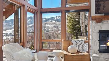Une pièce chaleureuse avec de grandes fenêtres donnant sur les montagnes, une cheminée et des fauteuils confortables.