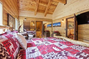 A log cabin interior with a large bed, wooden walls, a staircase, and a television.