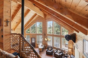 A wooden cabin interior with a dining area, seating, and a large window overlooking trees. - Wonderful 4-bedroom cabin in charming Duck Creek Village (Duck Creek Village)