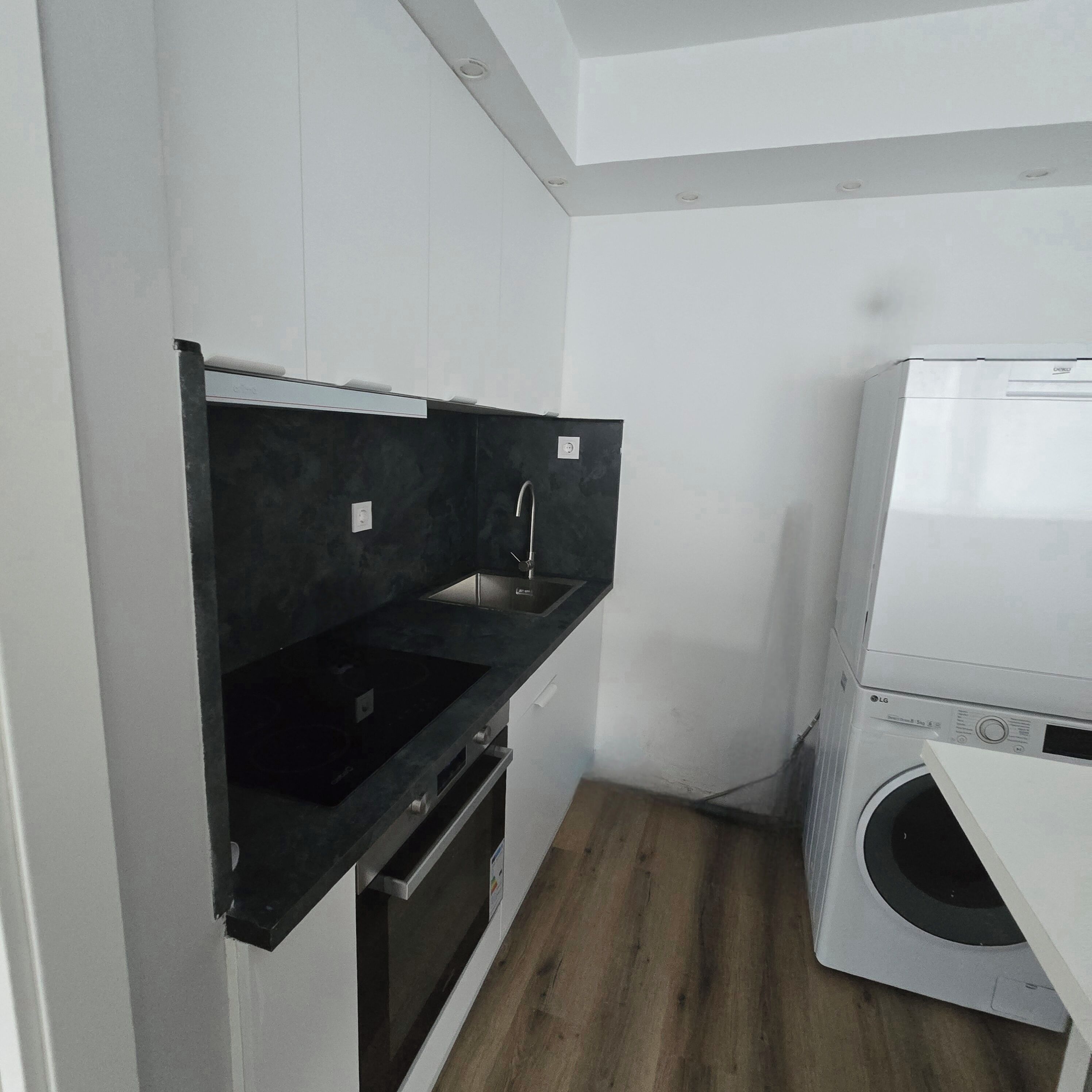 Una cocina compacta con horno integrado, un lavabo y una lavadora.