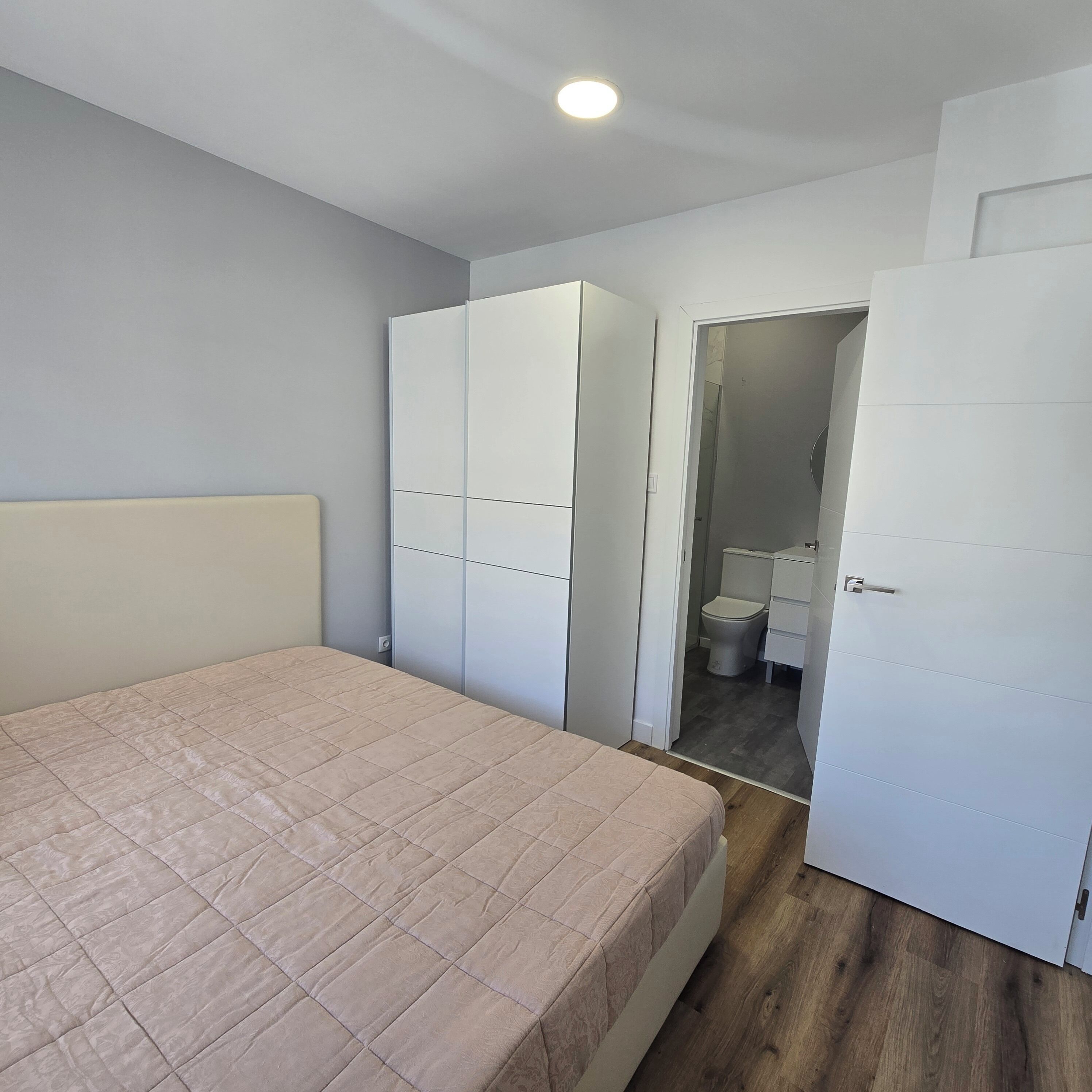 Une chambre à coucher avec un lit, une armoire et une salle de bain visible à travers une porte ouverte.