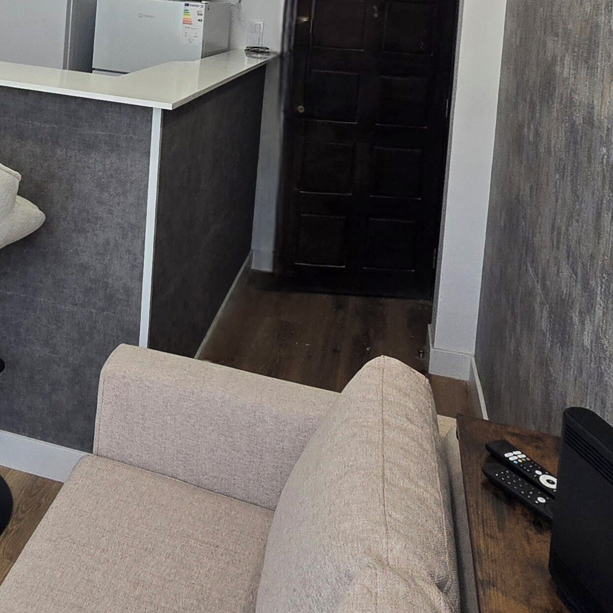 A modern living room with a sofa, a coffee table, and a TV. There is a door leading to another room.