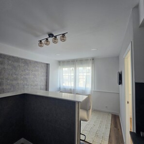 A modern room with a dark accent wall, a white desk, a chair, a large window with sheer curtains, and a ceiling light fixture. - Premium renovated 1 BR apartment in hiatoric downtown (Porto)