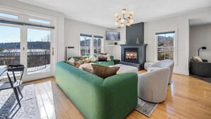 Un moderno salón con un sofá seccional verde, una chimenea y un ventanal con vistas panorámicas.