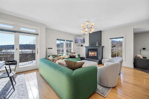 Ein modernes Wohnzimmer mit einem grünen modularen Sofa, einem Kamin und einem großen Fenster mit Blick auf eine schöne Landschaft.