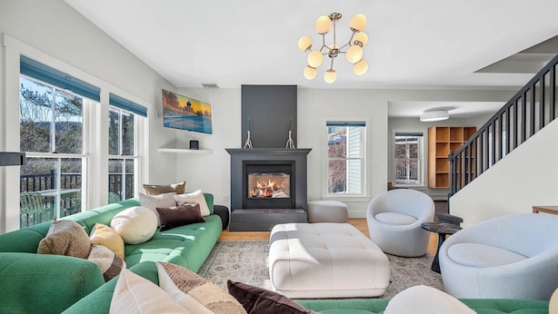 Una sala de estar moderna con chimenea, sofás verdes y una escalera.