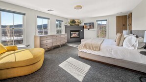 Un dormitorio moderno con una cama grande, un sillón amarillo, una chimenea y ventanas amplias que dan al exterior.