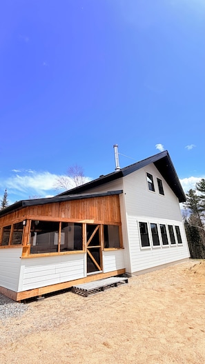 A two-story house with a large porch, a chimney, and a gravel driveway.