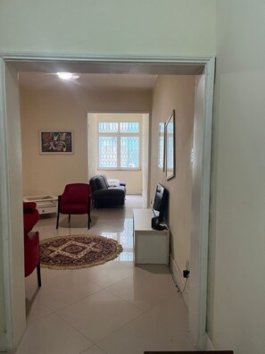 A living room with a TV, a sofa, a red chair, a rug, and a window with decorative glass. - Apartment for rent (Rio de Janeiro)