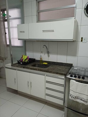 A kitchen with white cabinets, a granite countertop, a stainless steel stove, and a window with blinds. - Apartment for rent (Rio de Janeiro)
