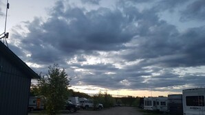 A campground with RVs parked on a gravel path, a small building on the left, and a cloudy sky.