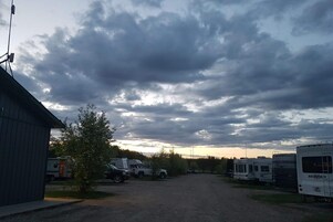 A campground with RVs parked on a gravel path, a small building on the left, and a cloudy sky.