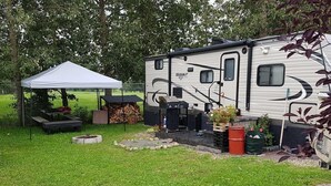A recreational vehicle with a covered outdoor area, a grill, and a fire pit.